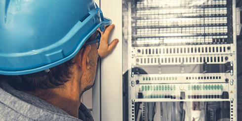 Man observes machinery with an ipad in hand, wearing a construction hat and vest on the left hand side of the image. 