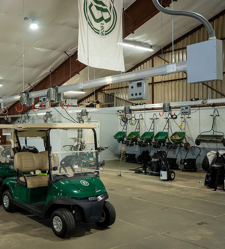 Gold carts parked in a garage charging via a Track Busway hanging overhead